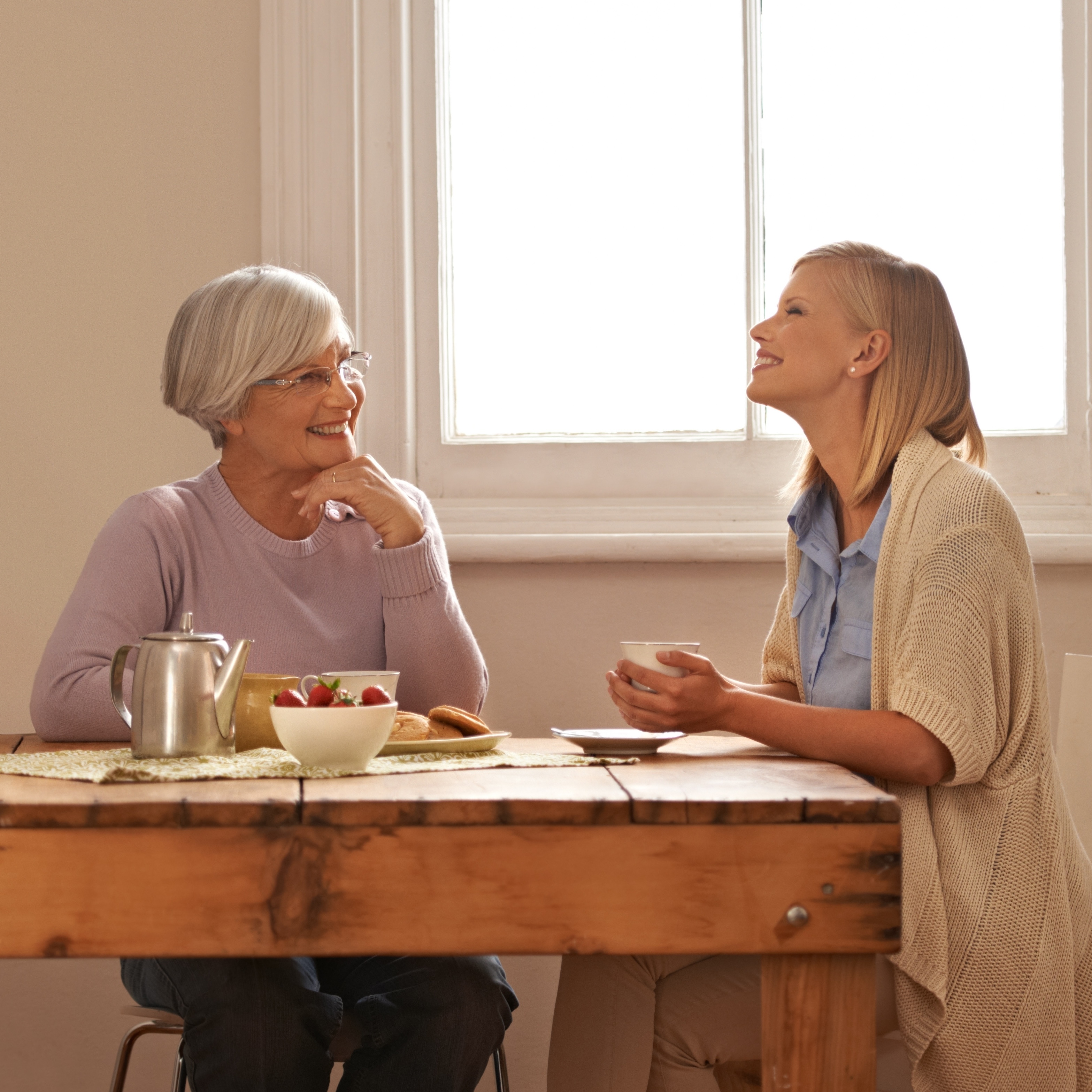 Family, happy woman and senior mother drinking coffee at breakfast, bonding and smile. Elderly mom, adult and tea cup at table for conversation, love and daughter eating cookies at home together